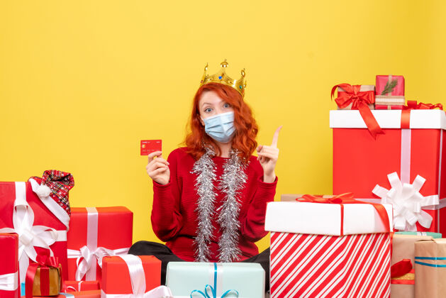 银行正面图是一位年轻女子戴着面具围坐在礼物旁边 黄色的墙上挂着银行卡年轻女性人圣诞节