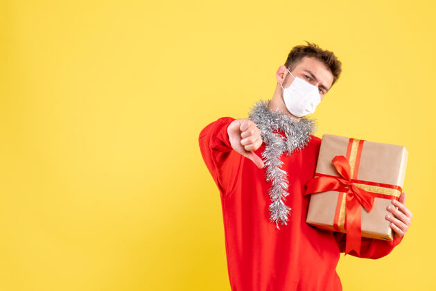 礼物正面图：戴着无菌面具的年轻男性正在过圣诞节年持有颜色