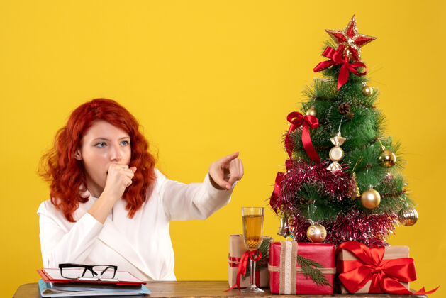 礼物女工人坐在桌子后面 手里拿着圣诞礼物和黄色的圣诞树女漂亮工人