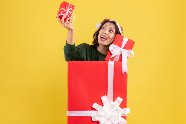 人站在盒子里的年轻女子的正面图 黄色的墙上有圣诞礼物前面里面快乐