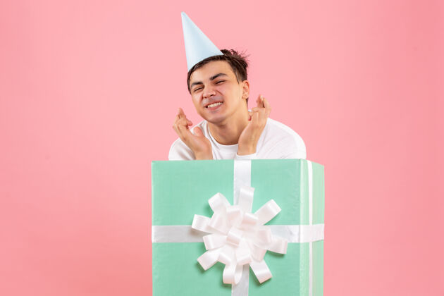 前面一个年轻人躲在粉红色的墙上礼物的正面视图礼盒微笑庆祝