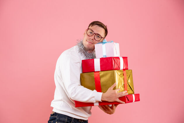 礼物一个年轻人在粉红色的墙上拿着圣诞礼物的正面图礼物人类礼品盒