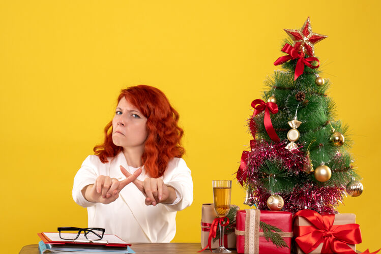 树女工人坐在桌子后面 手里拿着圣诞礼物和黄色的圣诞树礼物女工人情感