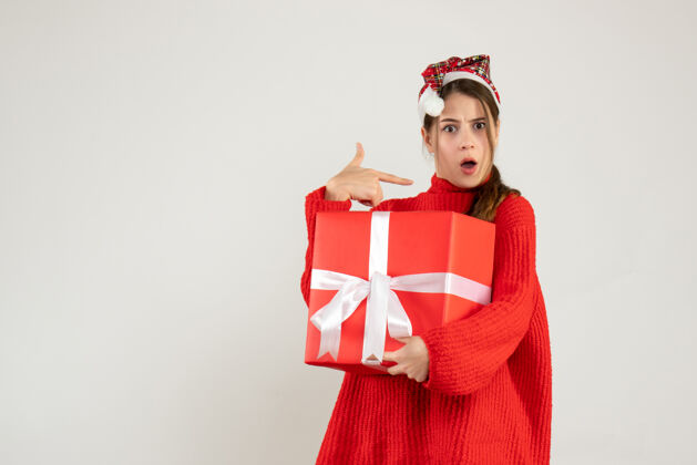 圣诞老人一个戴着圣诞帽的女孩拿着礼物 手指指着站在白色地板上的自己惊讶欢乐礼物