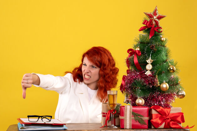情感女工人坐在桌子后面 手里拿着圣诞礼物和黄色的圣诞树礼物人圣诞节