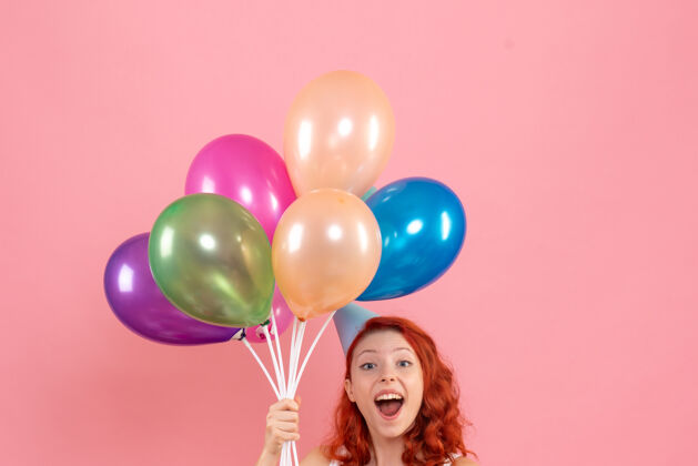 年轻粉红色墙上手持彩色气球的年轻女子的正视图女人纸五颜六色