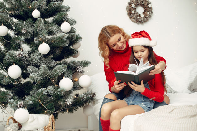 圣诞老人人们在为圣诞节做准备母亲在和女儿玩耍一家人在节日的房间里休息孩子穿着红色毛衣毛衣杉木帽子
