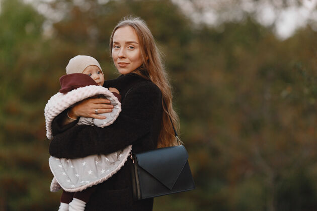 树叶时尚的母亲带着女儿人们走在外面穿着黑色夹克的女人帽子女儿户外