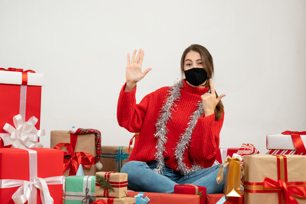 圣诞节穿着红色毛衣 戴着黑色面具的年轻女孩在白色的礼物上围坐着做枪牌面具枪年轻