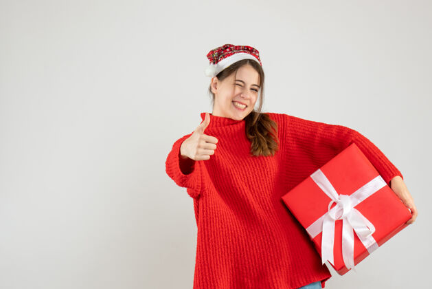 圣诞老人戴着圣诞帽的快乐女孩做了个竖起大拇指的牌子 拿着白色的礼物男性人使