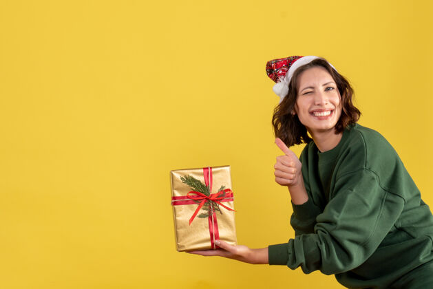 快乐黄色墙上拿着小圣诞礼物的年轻女子的正视图聚会年轻女性情感