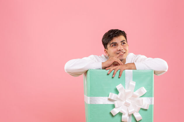 人隐藏在粉红色墙上的礼物里面的年轻人的正面视图圣诞节微笑礼品盒