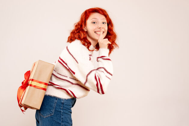 情感前视图的年轻女子隐藏圣诞礼物背后 她在白墙礼品盒庆祝十二月