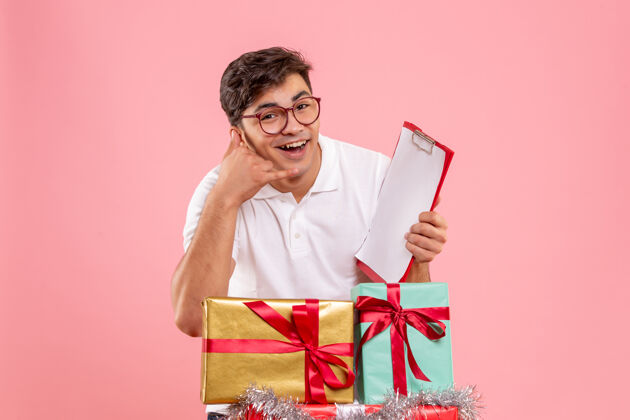 礼品盒年轻人在圣诞节前后的正面图 粉红色墙上拿着文件纸条节日成人礼物