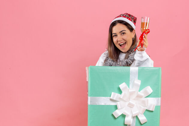 快乐前视图的年轻女子庆祝圣诞节与饮料上粉红色的墙壁饮料礼品盒微笑
