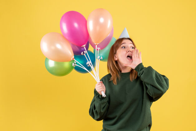年轻的女性正面图：带着彩色气球的年轻女性吹生日庆祝