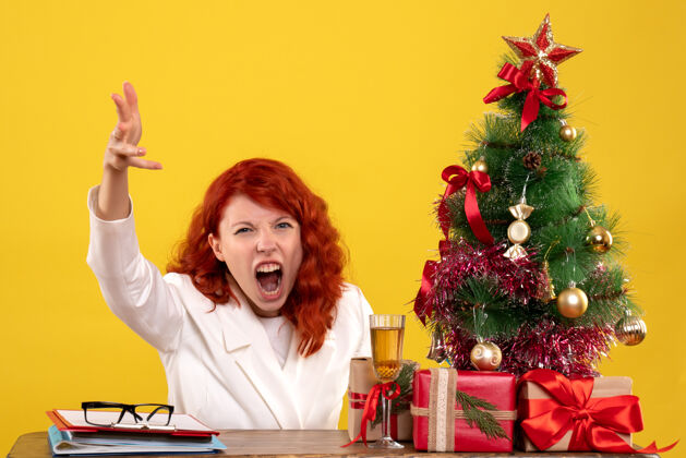 女女工人坐在桌子后面 手里拿着圣诞礼物和黄色的圣诞树情感工人黄色