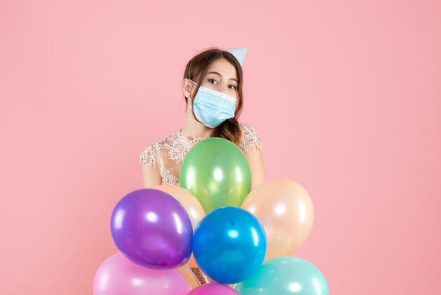 气球戴着派对帽和医用面具的派对女孩手里拿着粉色的彩色气球五彩纸屑气球医疗