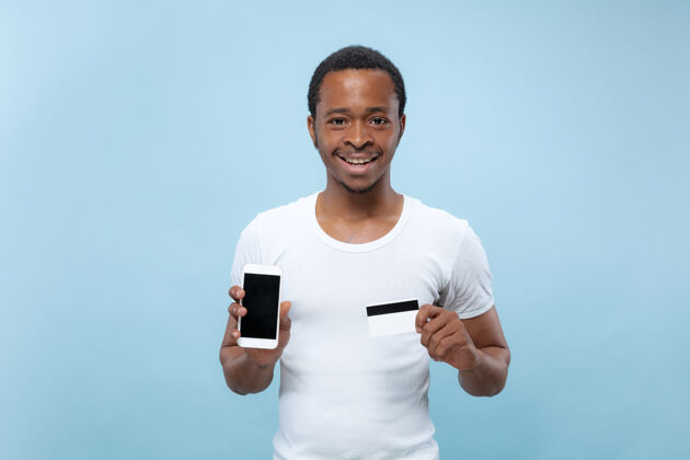 信用卡一个身穿白衬衫 手持卡片和智能手机的年轻非裔美国人的肖像年轻人卡