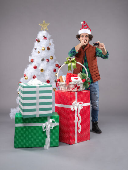 圣诞老人年轻的男性在灰色的圣诞礼物周围帽子圣诞圣诞树