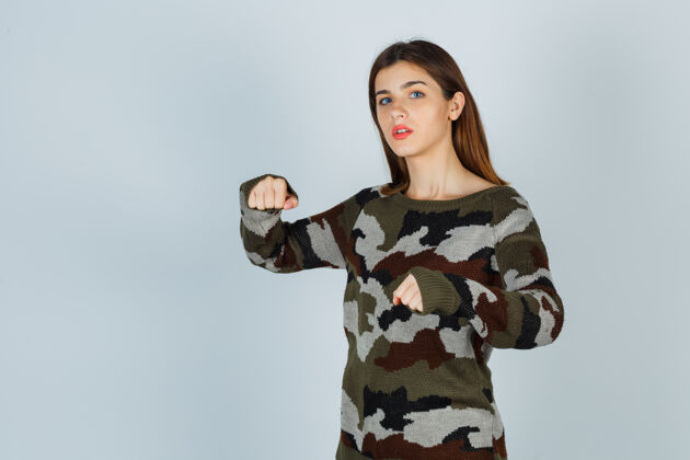 焦点年轻的女士站在战斗的姿势在毛衣 裙子和看起来自信肖像自然裙子