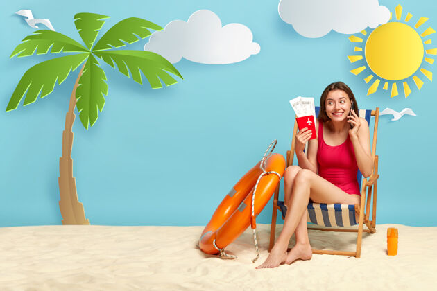 享受快乐的女孩在沙滩上晒日光浴 在阳光躺椅前摆姿势 讲手机 拿着护照和票 享受暑假手机快乐电话
