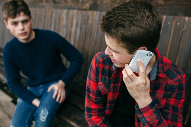 放松穿着格子衬衫的年轻人在用智能手机说话男性坐着朋友