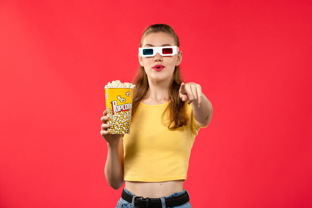 年轻女性前视图年轻女性手持爆米花包在-d太阳镜上的浅红色墙壁影院电影女孩电影爆米花制造护目镜