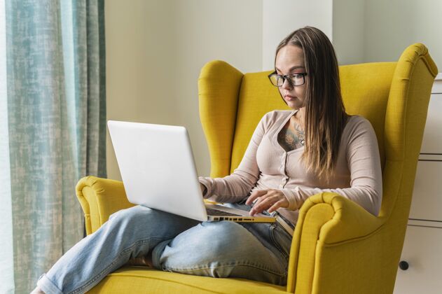 流行病流感大流行期间 一名妇女在家里的扶手椅上操作笔记本电脑冠状病毒预防隔离