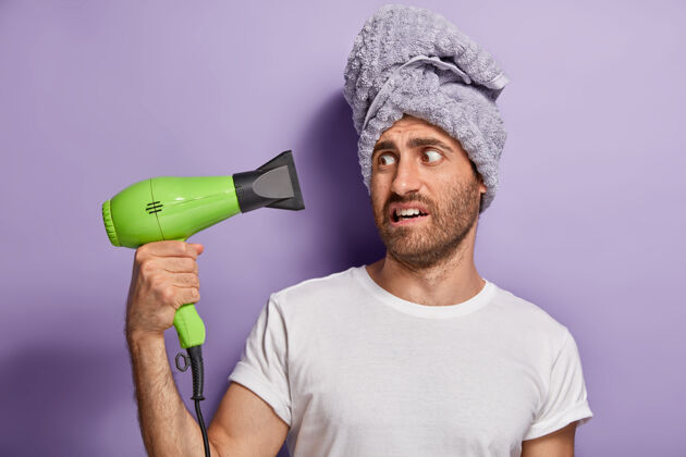 不高兴我的电吹风出毛病了沮丧的男人吹干头发 头上戴毛巾 早上做美容男性未刮胡子空气