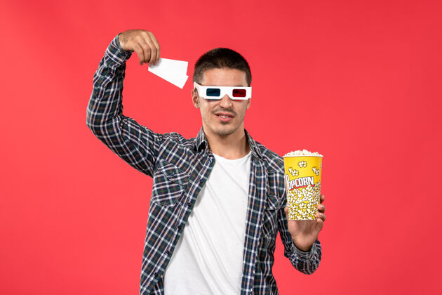 年轻男性正面图手持爆米花票的年轻男性戴着d型太阳镜在浅红色的墙上看男性电影男人剧院成人