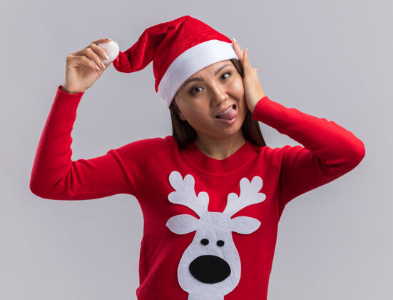 年轻快乐的年轻亚洲女孩戴着圣诞帽和毛衣 在白色背景上露出孤立的舌头快乐圣诞节毛衣