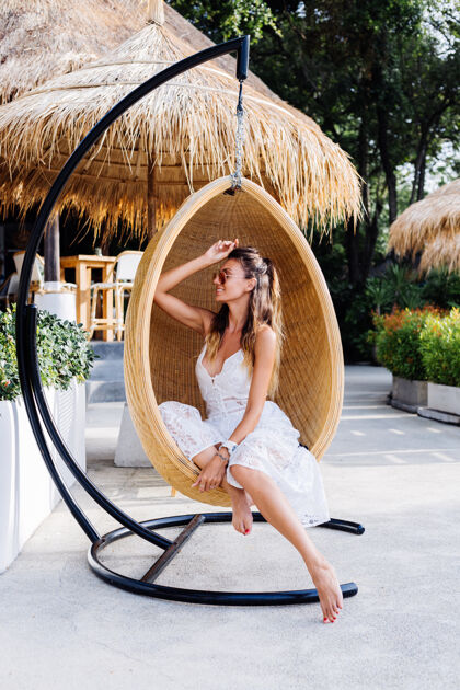 度假穿着白色夏装的欧洲浪漫女人在度假酒店外鸡蛋草椅上的画像皮肤年轻独自