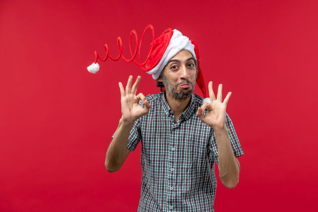 人红墙上戴着滑稽玩具帽的年轻人的正视图快乐圣诞节年轻