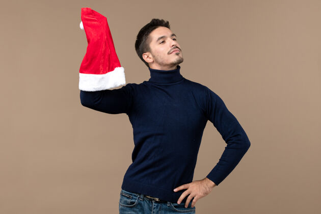 成人正面图：年轻男子在棕色背景下玩红帽子圣诞节情感假期背景帽子肖像