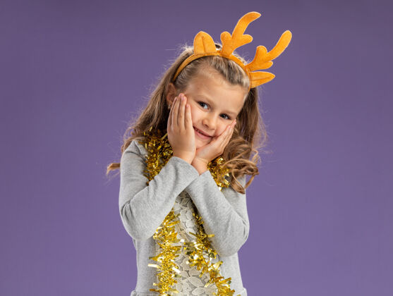 脖子高兴的小女孩戴着圣诞发箍 脖子上戴着花环 两颊被蓝色背景隔离开来箍高兴小