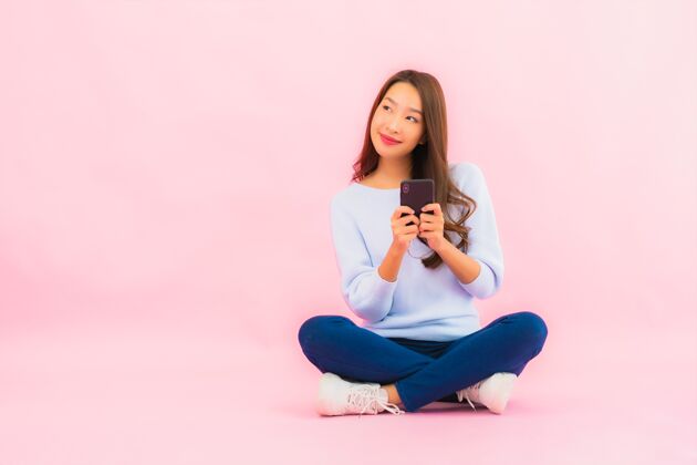 信息肖像美丽的亚洲年轻女子在粉色隔离墙上使用智能手机年轻女士手机