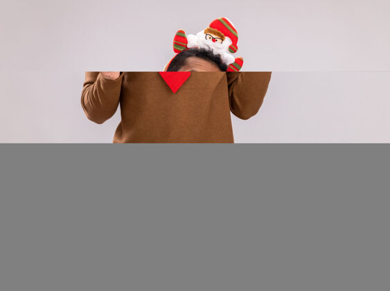 手杖快乐的非洲裔美国人 身穿棕色毛衣 头戴圣诞老人戒指 打着有趣的红色领带 手持糖果手杖 站在白色背景下 看着摄像机 开心地微笑着微笑领带圣诞老人