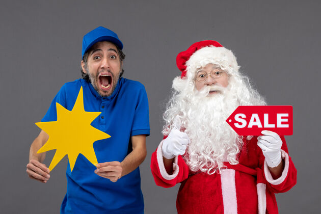 快乐圣诞老人的正面图 男性信使手持销售横幅 灰色墙上有黄色标志男圣诞人