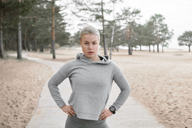 跑步自信运动的金发美女 短发 双手放在户外 在有氧运动中休息片刻漂亮的女跑步者 穿着时髦的衣服 在公园里训练慢跑跑步者身体