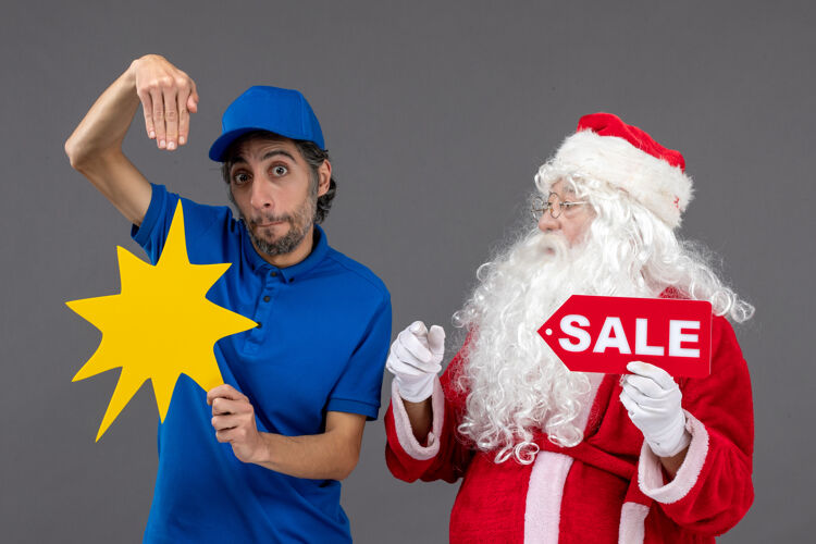 快乐圣诞老人的正面图 男性信使手持销售横幅 灰色墙上有黄色标志圣诞老人圣诞销售