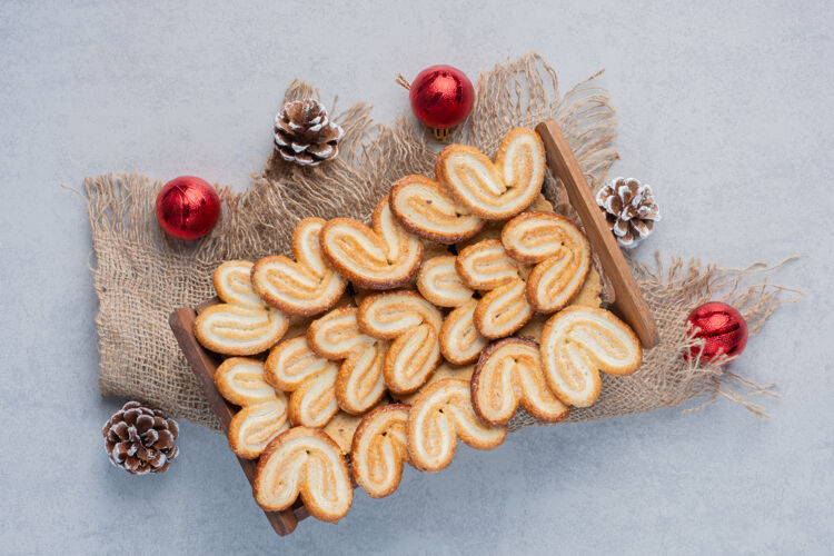 美味一堆圣诞装饰品围绕着片状饼干堆在大理石表面的木篮里糖美味圣诞节
