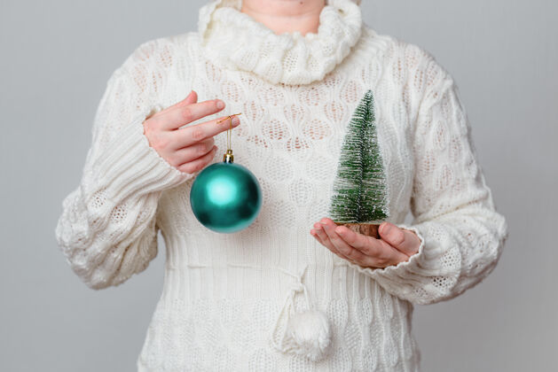 庆祝穿着白色毛衣的女人拿着一个绿松石色的圣诞球和一棵微型松树传统小女性