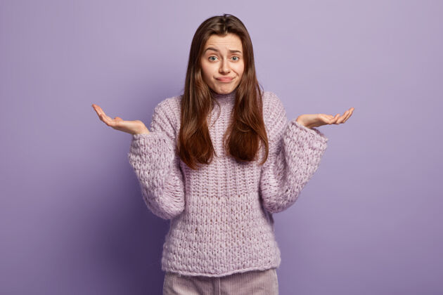 面部生活感知概念不知情的欧洲女性耸耸肩 做决定 穿着紫罗兰色的毛衣 有着犹豫不决的表情 站在和手势中 隔着紫色的墙壁不知道为什么困惑