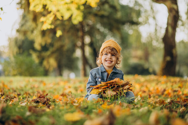 黄色帽子可爱的男孩在秋天公园玩树叶瞬间甜蜜可爱
