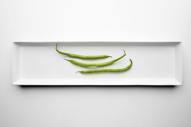 景观三颗绿豆隔离在长方形白色陶瓷板中间的桌子上营养豆类菜