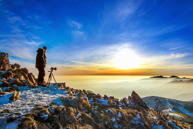 早晨日落时分 专业摄影师用相机在岩石峰的三脚架上拍照山谷峰雾