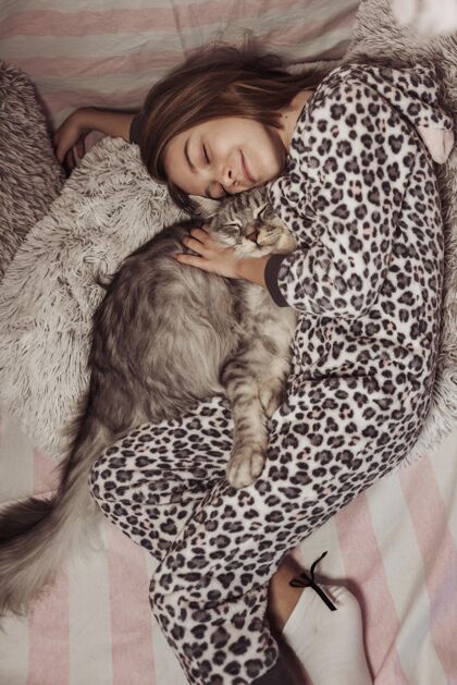动物穿着睡衣的女孩抱着她的猫躺在床上孩子可爱小猫