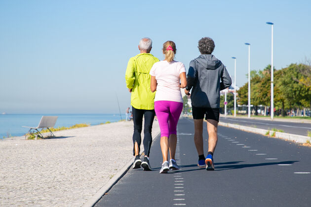 后部穿着运动服的成熟慢跑者的后视图沿着河岸在跑道上跑步全长 复制空间活动或健康的生活方式概念退休运动头发