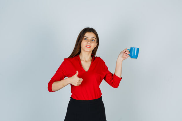 专业一位年轻的女士拿着杯子 穿着红色上衣 裙子 竖起大拇指 看上去很自信快乐成功积极
